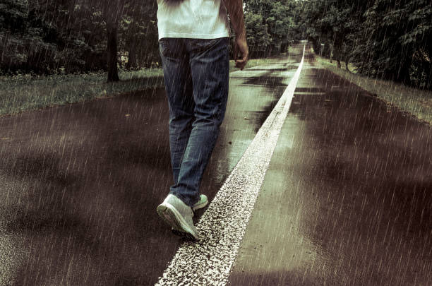 A man walking alone in the rain on a park alley
