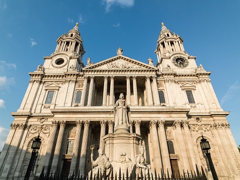 Low angle view of St Paul's Cathedral in London, United Kingdom. The sky is blue with high clouds. The main entrance and statue of Queen Victoria is in view. Shot with a medium format camera and a wide angle lens.