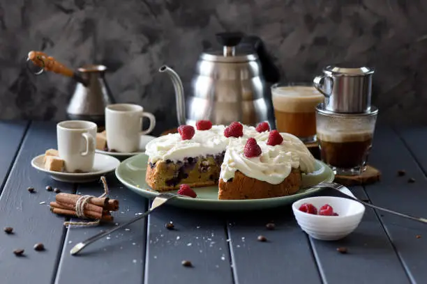 Healthy low sugar fruit cake with coconut cream roses and raspberries served with black coffee on dark background copy space. Still life with natural lighting scene