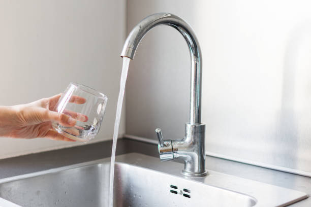 自宅の台所の流しで水のコップを取って台所で手。 - water faucet running water glass ストックフォトと画像