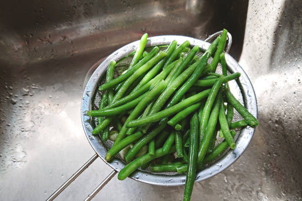 Washed raw green beans in mesh strainer in sink of kitchen