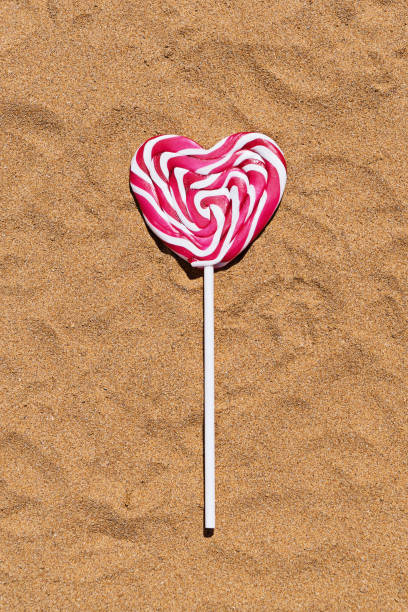 zbliżenie różowego lizaka w kształcie serca na piasku, falt lay view - beach love heart shape two objects zdjęcia i obrazy z banku zdjęć