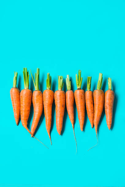 istock several fresh carrots lie in a row on a blue background. 1171746043