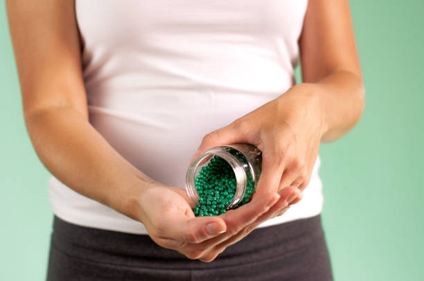 una chica embarazada le echa pastillas de un frasco en la mano. concepto de protección de la salud maternoinfantil. - twin tips fotografías e imágenes de stock