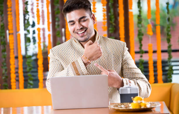 Raksha bandhan celebration Man showing rakhi on his wrist while doing video chat using laptop on raksha bandhan festival rakhi stock pictures, royalty-free photos & images