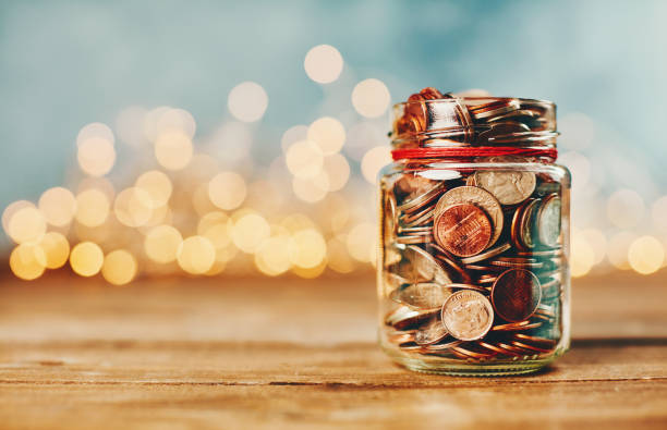 spendengeld-glas gefüllt mit münzen vor feiertagsbeleuchtung - finanzen und wirtschaft fotos stock-fotos und bilder