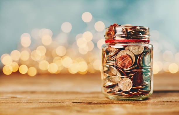 Donation money jar filled with coins in front of holiday lights Donation money jar filled with coins in front of holiday lights giving money stock pictures, royalty-free photos & images