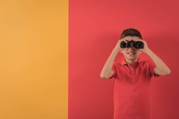 маленький мальчик с помощью бинокля перед цветной стеной - little boys discovery binoculars child стоковые фото и изображения