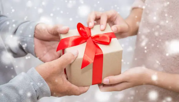 Photo of Close up hands of senior old man and his daughter giving gift box with snow background. Boxing day holiday birthday christmas day concept