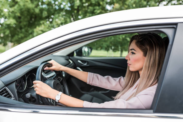 Woman driving a car, long hair, serious look, in summer in the passenger compartment of a white business class car. Business lady goes to work. stock photo