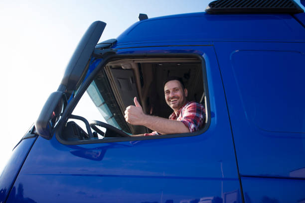водитель грузовика показывает большие пальцы вверх через окно кабины. позитивный улыбающийся дальнобойщик готов к новой поездке. транспор - truck semi truck blue truck driver стоковые фото и изображения