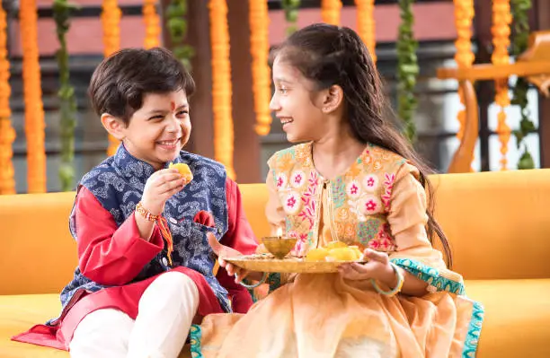 Little brother feeding sweet food to his sister on the occasion of Raksha Bandhan festival