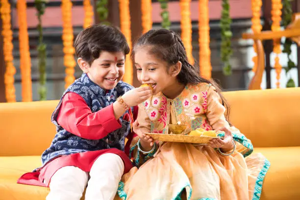 Little brother feeding sweet food to his sister on the occasion of Raksha Bandhan festival