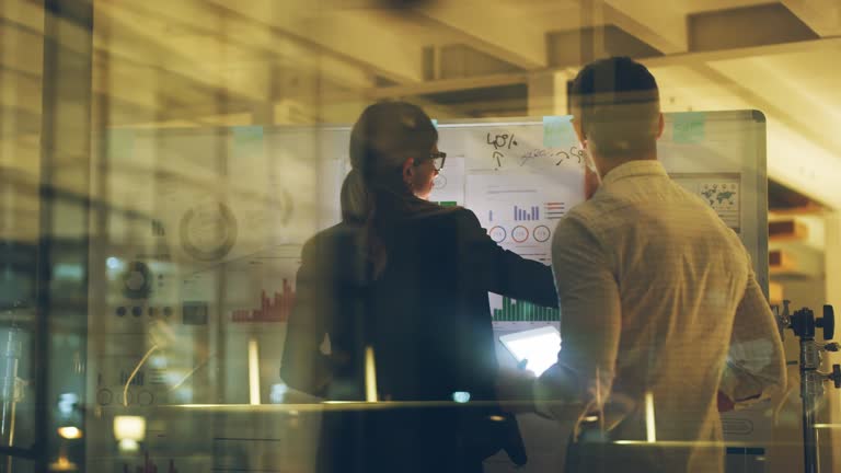 4k video footage of two businesspeople planning and brainstorming ideas on a whiteboard while working late together in their office