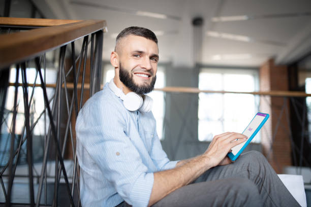 istock Bearded man with earphones on neck holding little tablet 1171780988