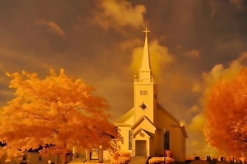 A small country christian church at dusk with cumulus storm clouds gathering for an evening rain.  Taken using IR camera with color manipulation to achieve the effects seen.