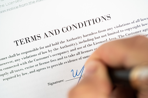 Close up hand with pen on the signature line on a terms and conditions agreement busy signing