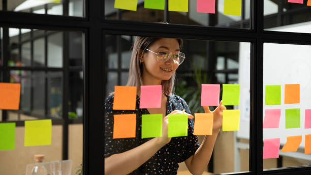 istock Smiling asian businesswoman write tasks on sticky notes on glass wall 1171786296