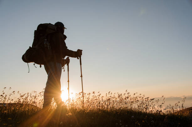istock Man standing on the hill with hiking backpack and sticks looking at the sunset 1171787339
