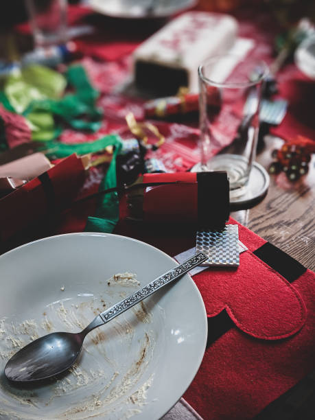 Dark vintage filter effects applied for artistic effects. Empty plate with spoon and leftover Christmas cake on a messy table after the party. Vertical.