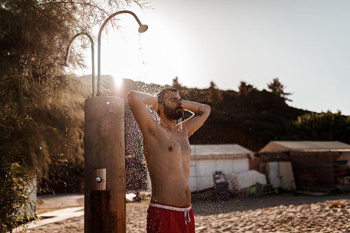 Handsome bearded man showering at the beach on a sunny summer day during vacation in Greece