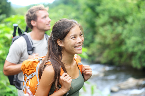 People hiking - happy hiker couple trekking as part of healthy lifestyle outdoors activity. Young multiracial couple walking in nature in Iao Valley State Park, Wailuku, Maui, Hawaii, USA.