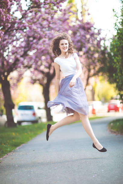 istock Young girl dancing and jumping under the blooming sakura trees. 1171791320