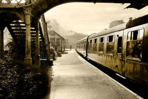Steam train at Sherringham Station, Norfolk, England, UK, black and white retrospective photograph of a steam train and carraiges at Weybourne station, Norfolk, England, UK, the platform is misty and in the distance is the gaurd and signal box passenger train photos stock pictures, royalty-free photos & images
