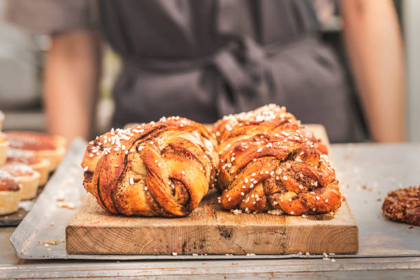 Twisted traditional Swedish cinnamon buns at a café Twisted traditional Swedish cinnamon buns at a café. The sweet buns are on a wooden chopping board, and there is an  unrecognizable person with an apron in the background. danish culture photos stock pictures, royalty-free photos & images