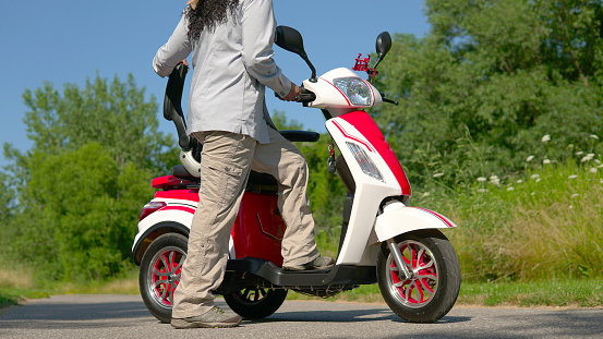 Woman standing near an electric scooter in the city park. Concept of driving ecological environmentally conscious power transport. Active adult lifestyle.
