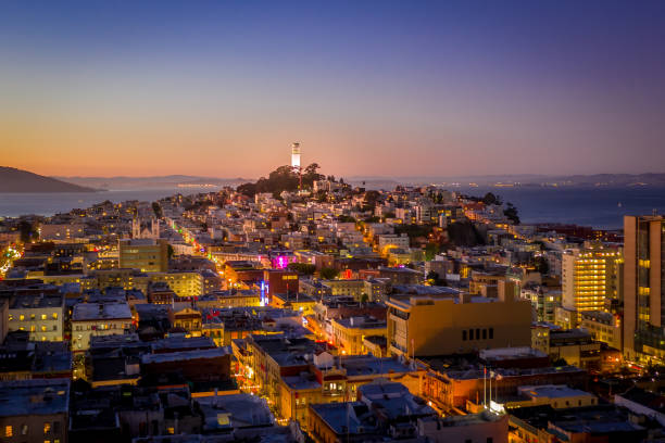 Aerial view across the city of Coit Tower at night with city lights sparkling across the sky. San Francosco Bay and in the background. View spns China town and North Beach.