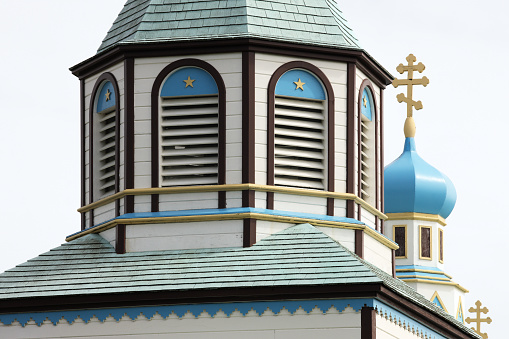 Holy Assumption of the Virgin Mary Church, a Russian Orthodox church in Kenai, Alaska built in 1895.  This image is a tight horizontal crop on the church spire with its light blue onion dome and yellow cross appearing from behind and a third yellow cross at lower right.