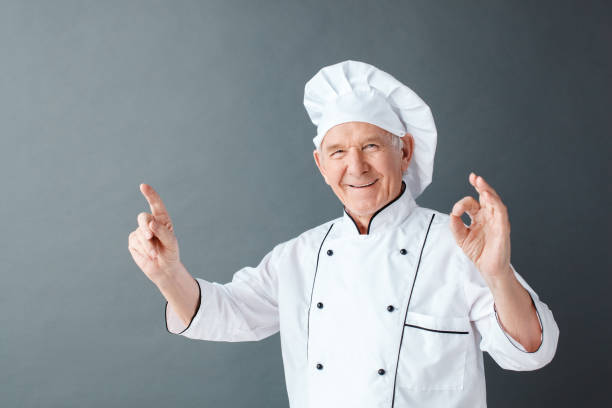 istock Senior chef studio standing isolated on gray pointing up showing ok sign smiling positive 1171824736