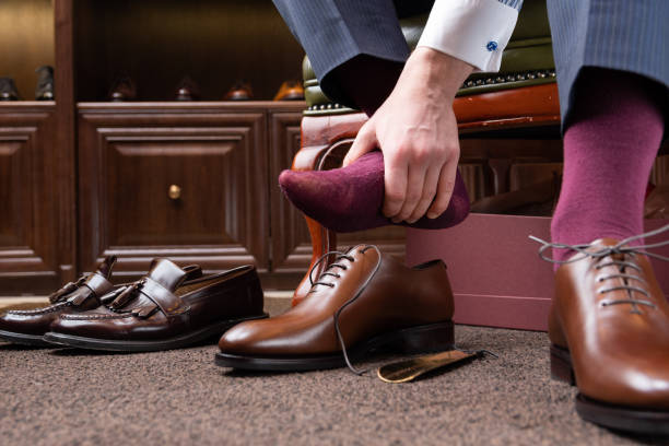 men shoes boutique store Trying new tight shoes. Man is putting on a new pair of luxury brown full grain leather shoes at footwear store and holding foot painfully. Old shoes left behind. brogue photos stock pictures, royalty-free photos & images