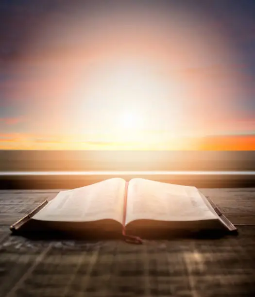 Photo of Close up of open Bible, with dramatic light. Wood table with sun rays coming through window. Christian image