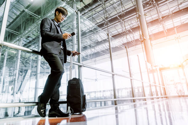 istock Businessman checking e-mail on mobile phone while walking with suitcase inside airport 1171836089