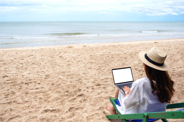 istock a woman using and typing on laptop computer with blank desktop screen while sitting on beach 1171841142