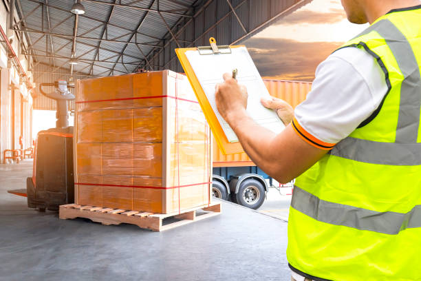 istock Warehouse and Logistics, freight transportation, worker in uniform hand holding clipboard inspecting details loading cargo with a trucks, electric forklift pallet jack with goods pallet at warehouse 1171845356