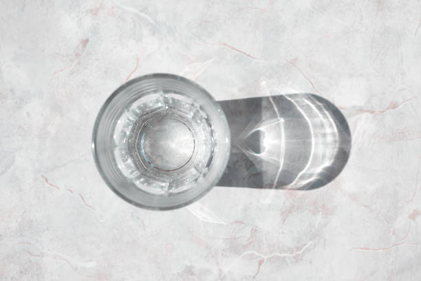 Glass of clear water on a white granite table in daylight, top view