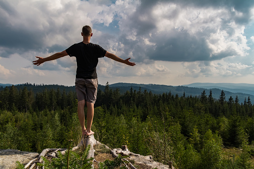 Young man meditating, stretching shoeless on tree stump, Sumava national park, Czech republic