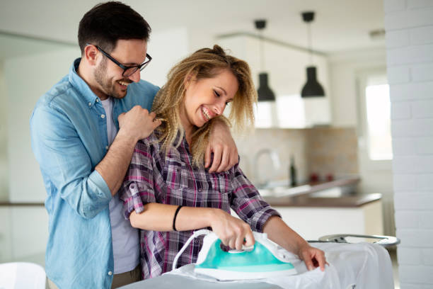 Happy young couple doing the ironing together Young couple doing the ironing together at home laundry husband housework men stock pictures, royalty-free photos & images