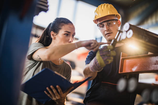 Female manager and manual worker measuring steel in industrial building. Young female foreman and her manual worker working on paperwork and steel in aluminum mill. metal industry stock pictures, royalty-free photos & images