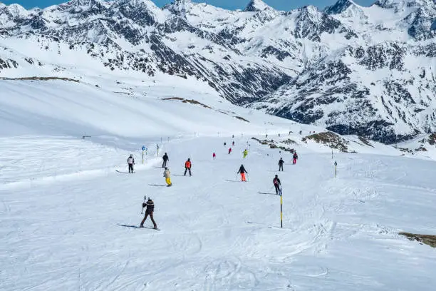 People skiing and snowboarding down a ski slope in the Sölden Ötztal ski area during a sunny winter day in the Tiroler Alps.