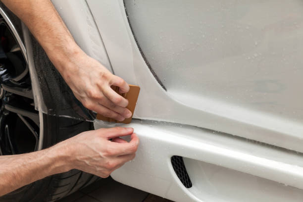 reacondicionando el coche con una sólida película protectora transparente, el maestro pega el recubrimiento protegiendo los vehículos de arañazos y virutas en el taller. - retrofitting fotografías e imágenes de stock