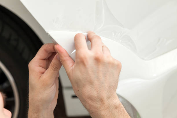 reacondicionando el coche con una sólida película protectora transparente, el maestro pega el recubrimiento protegiendo los vehículos de arañazos y virutas en el taller. - retrofitting fotografías e imágenes de stock