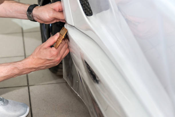 istock Retrofitting the car with a solid transparent protective film, the master glues the coating protecting the vehicles from scratches and chips in the workshop. 1171884941