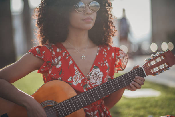 One woman, young and beautiful, sitting in park, playing acoustic guitar.