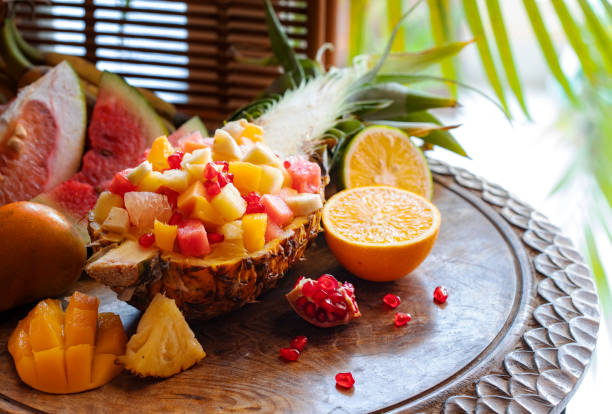 salade de fruits servie en demi-ananas sur une table en bois. concept de l'alimentation naturelle, alimentation saine, nutrition. ananas, mangue, pomelo, grenade, pastèque, banane, orange. - fruit exotique photos et images de collection