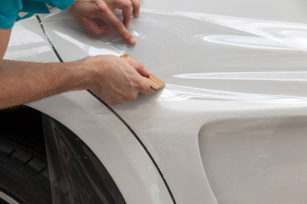 retrofitting o carro com uma película protetora transparente contínua, o mestre cola o revestimento que protege os veículos dos riscos e das microplaquetas na oficina. - retrofitting - fotografias e filmes do acervo