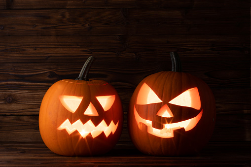 Two glowing Halloween pumpkins head jack lantern on old wooden background